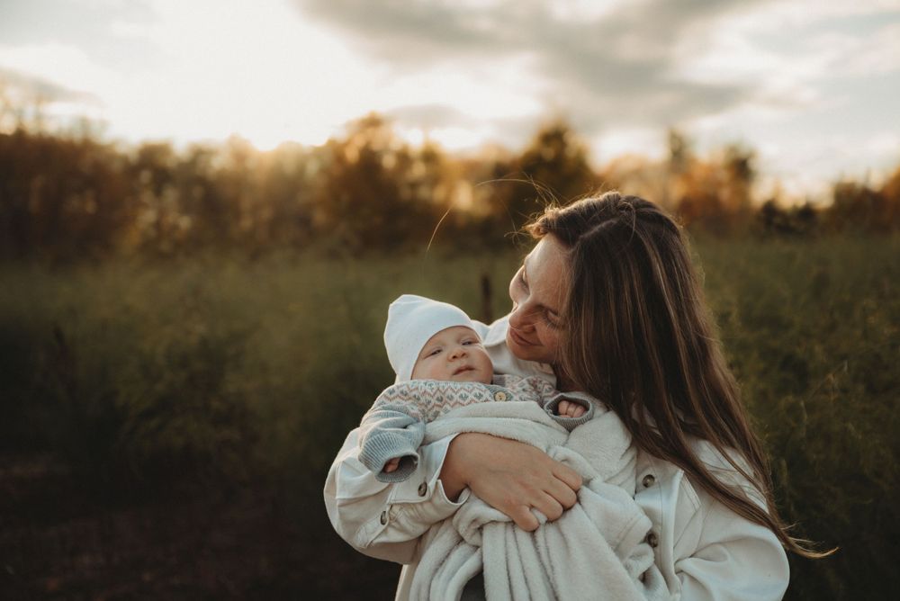 Intimate mother and baby moment captured in soft evening light outdoors.