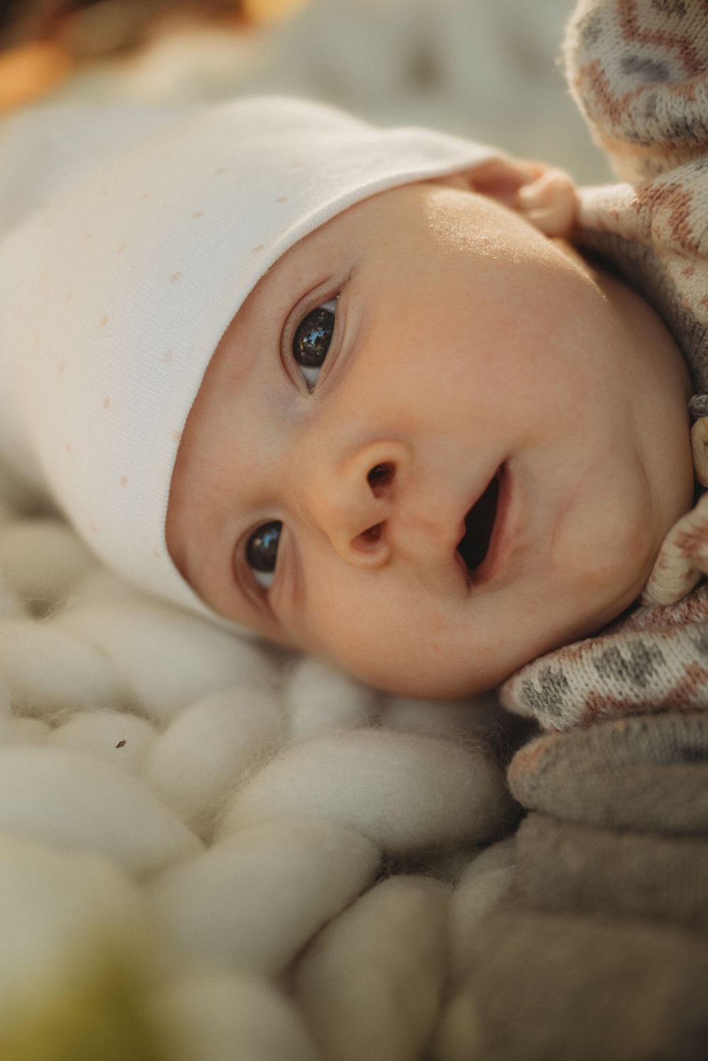 Close up of baby wearing white hat on textured knit blanket.
