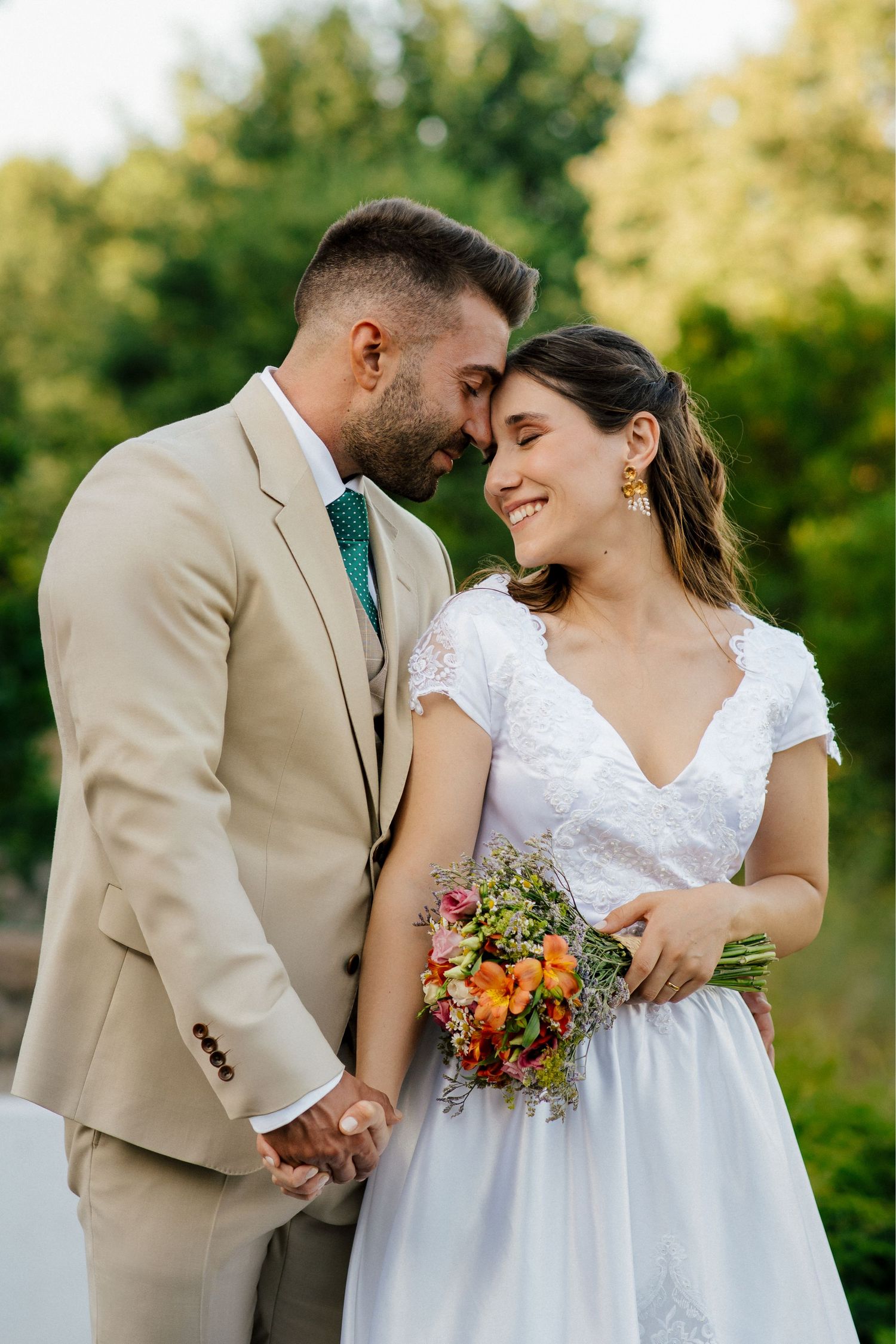 Couple shares intimate moment outdoors while holding colorful bouquet.