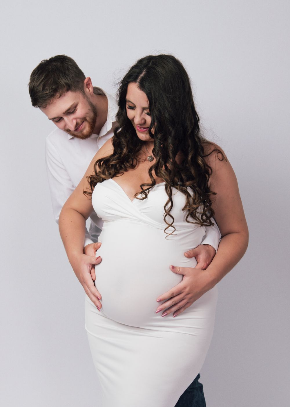 Beautiful pregnant woman posing in a field of wildflowers, wearing a flowing white dress. Maternity photoshoot in Spaldi
