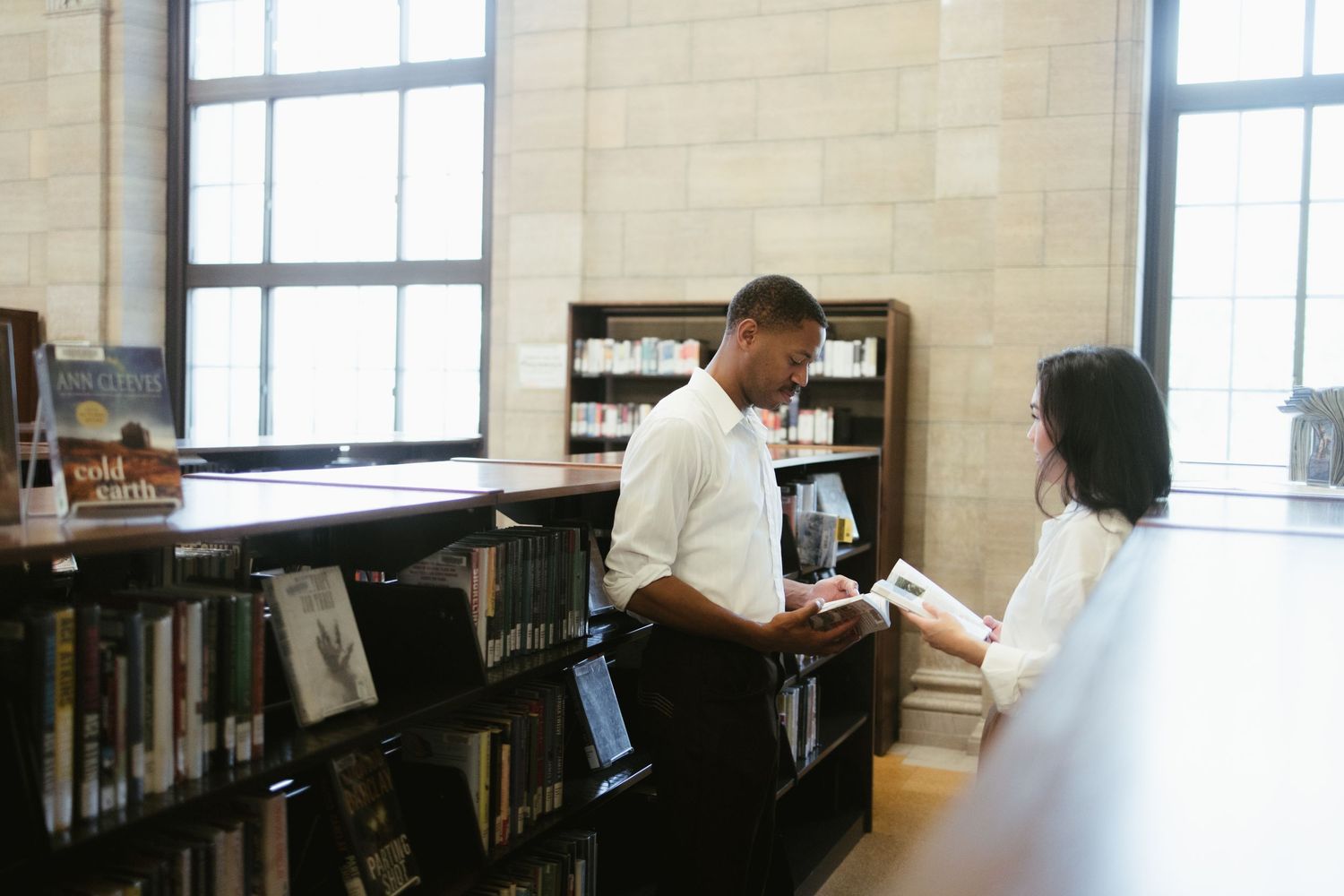 Candid moment of couple looking at books together in library setting.