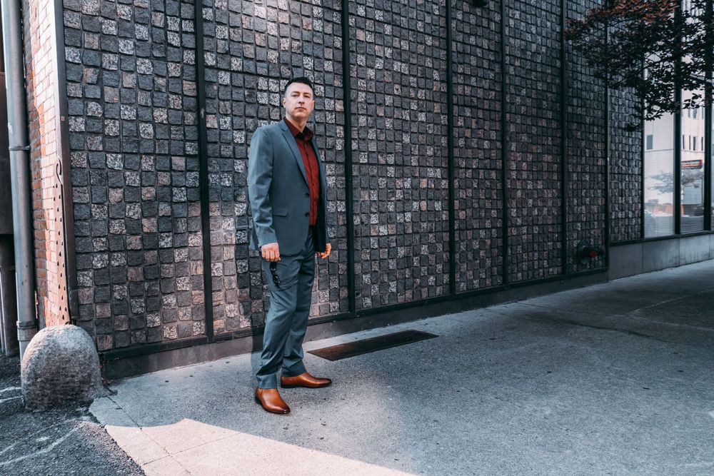 Full length fashion shot against textured brick wall featuring business attire and brown leather shoes.