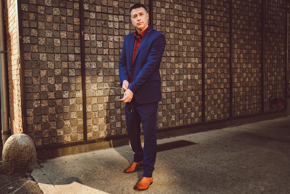 Street style fashion photograph featuring navy suit and brown shoes against textured wall.