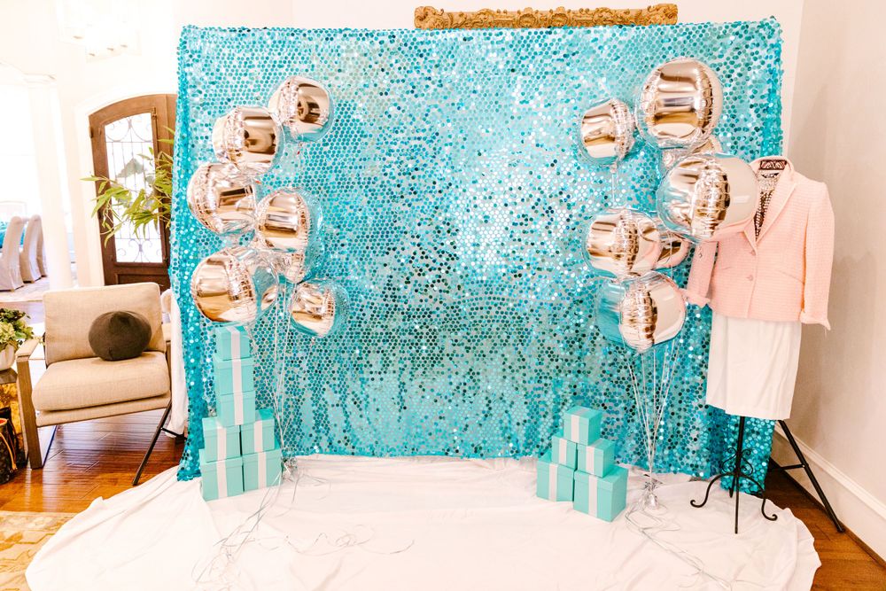 Glittering turquoise sequin backdrop with floating picture frames and pink clothing on a garment rack.