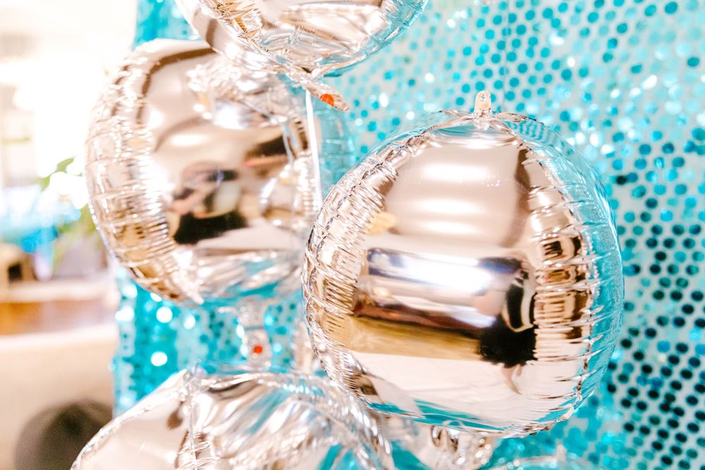 Close-up of shiny silver metallic Christmas ornament baubles against a sparkly turquoise background with bokeh effect.