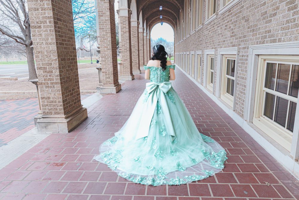 Person wearing an elegant mint green ball gown with a flowing train stands in a columned brick archway.