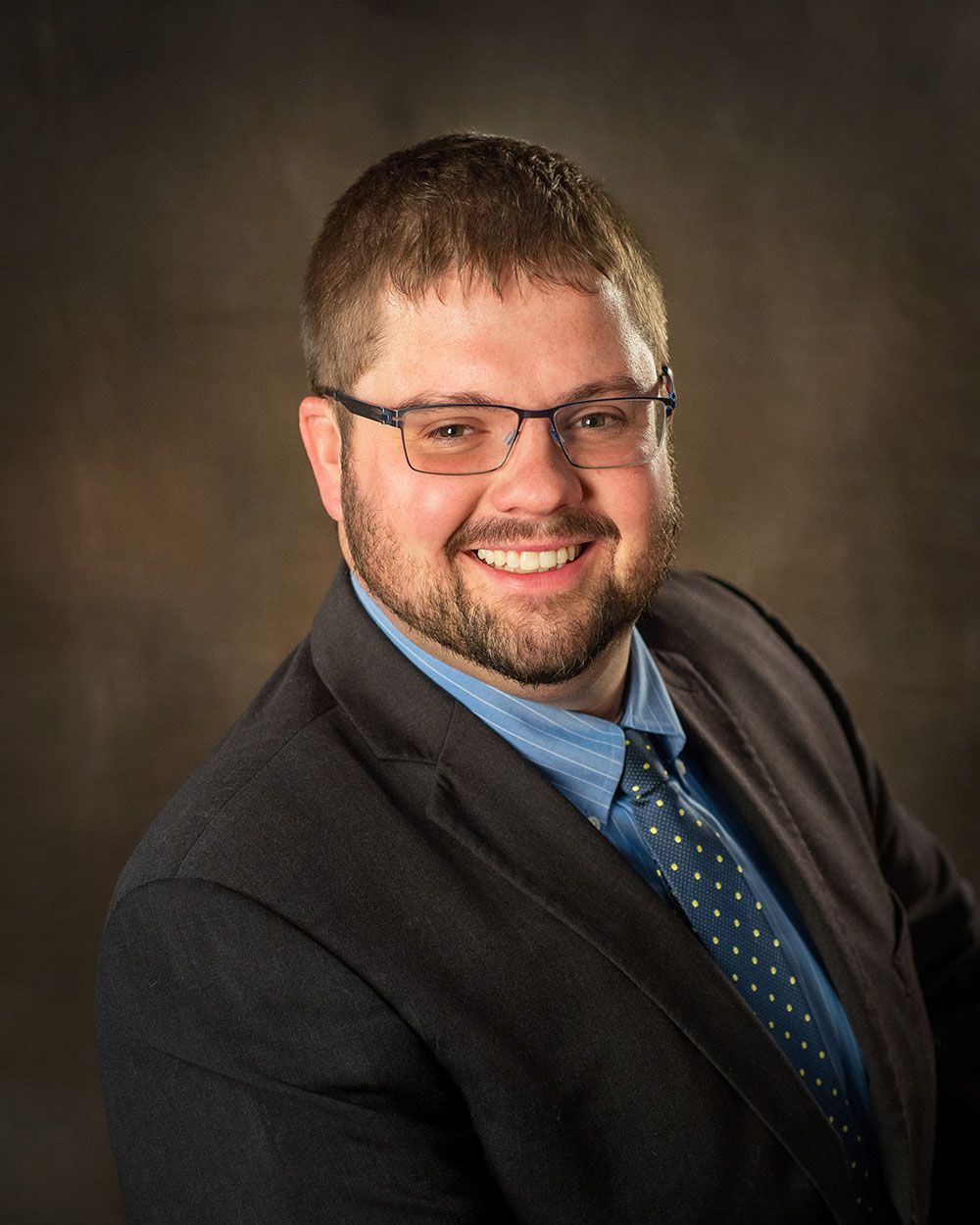 corporate headshot of a man in a suit with blue shirt and tie on a dark background backlighting by professional photographer Luba Wold