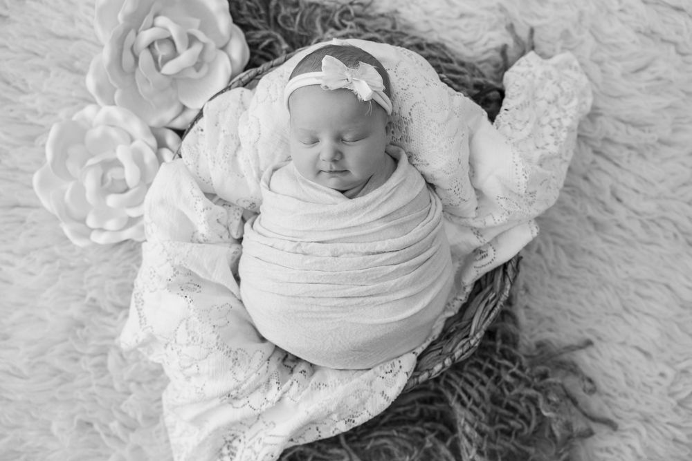 A series of black and white photographs showing a swaddled newborn baby lying on soft textured blankets.