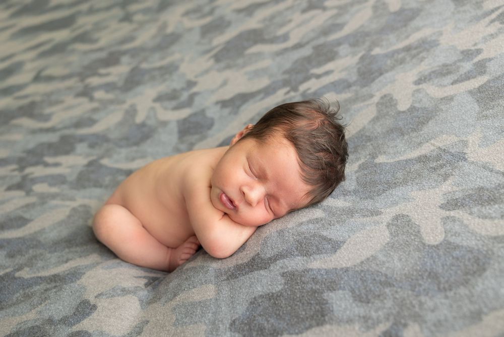 Peacefully sleeping newborn baby rests on soft gray patterned blanket during professional photo session.