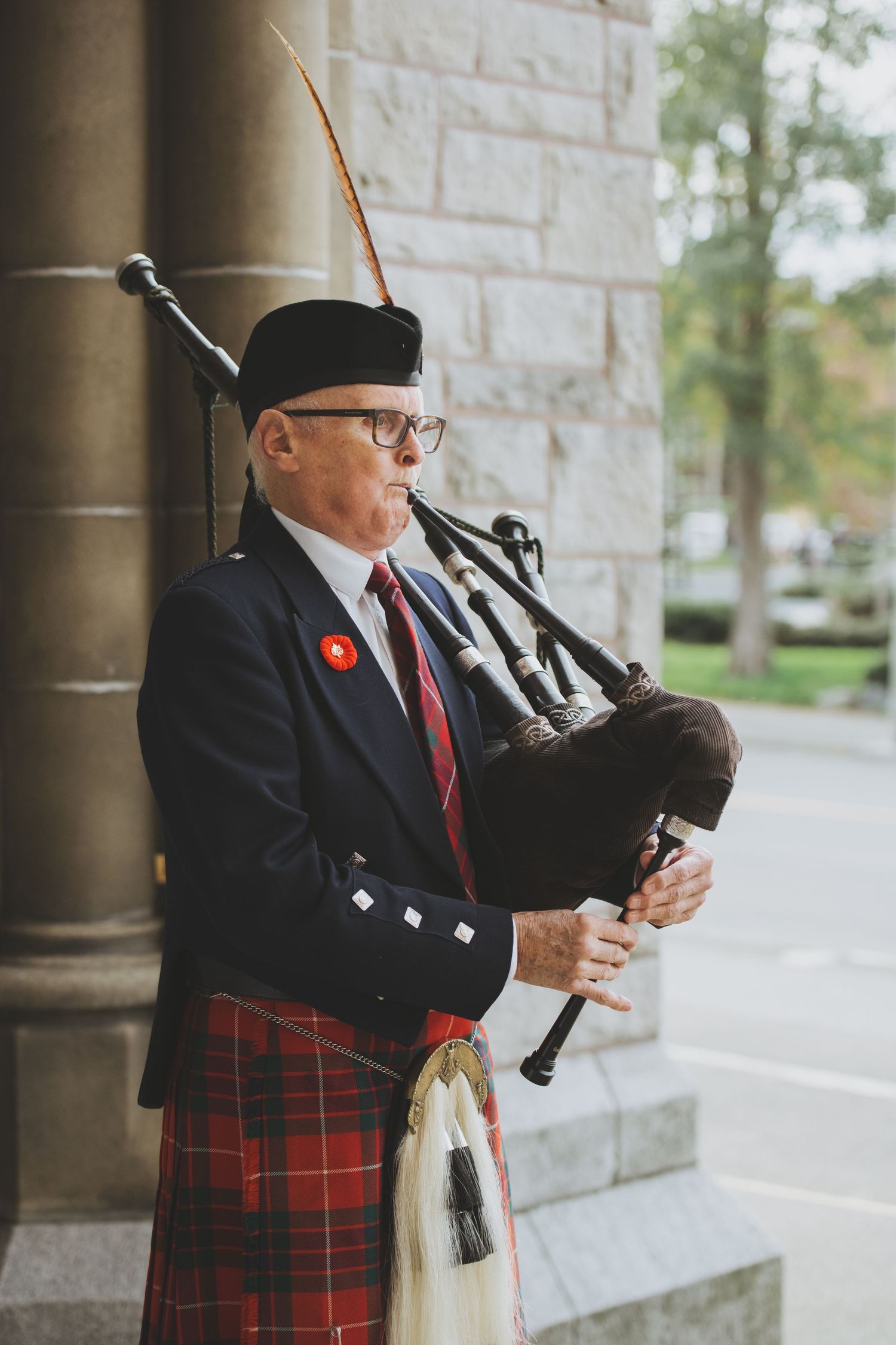 A bagpiper in traditional Scottish attire with red tartan kilt plays bagpipes outside the Christ Church Cathedral in Victoria, BC.