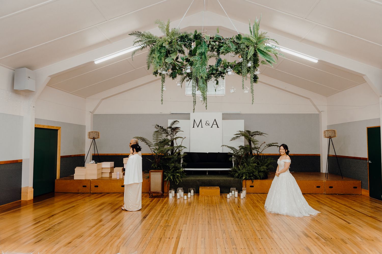Wedding venue interior with piano, greenery chandelier, and hardwood floors.
