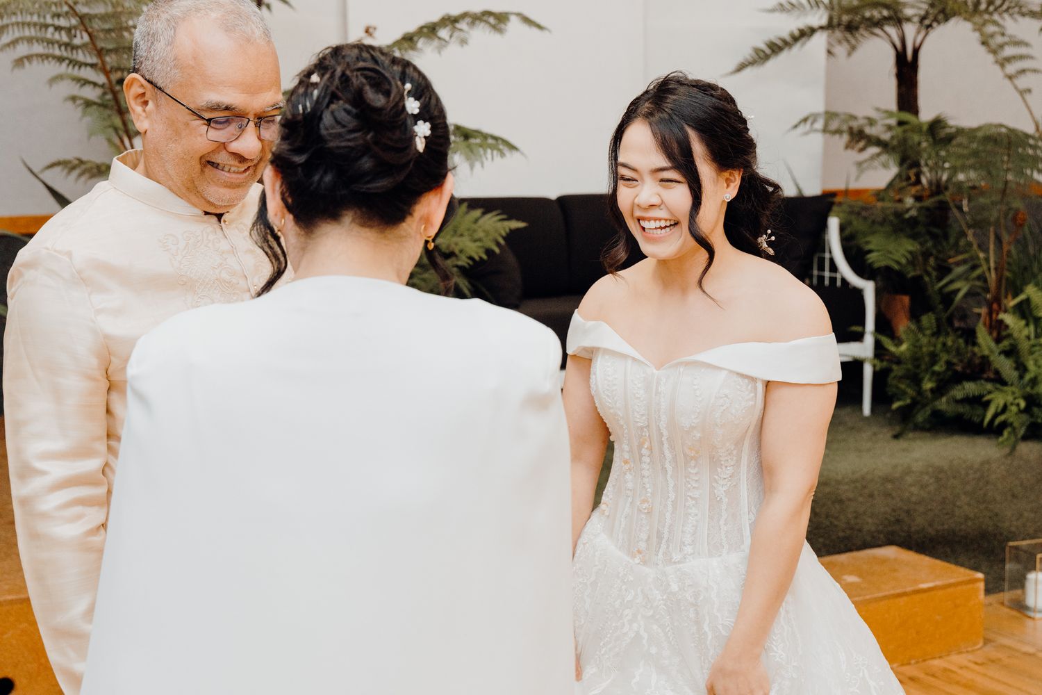Wedding ceremony scene with cream and white formal attire and fern decorations.
