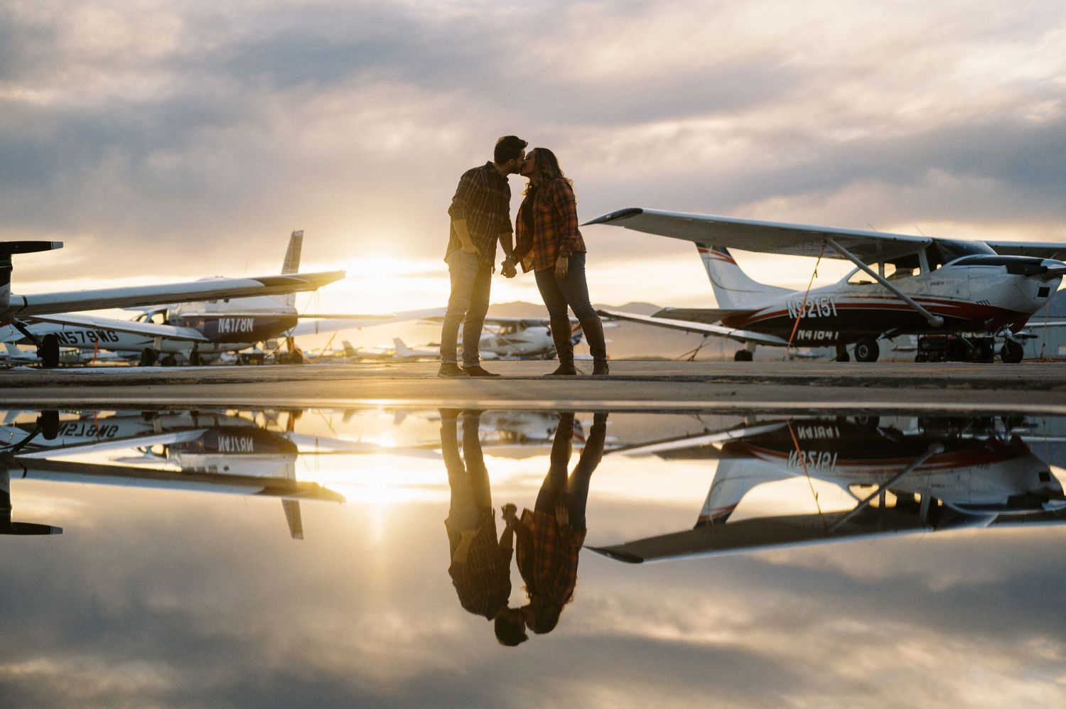 Silhouetted couple shares romantic moment between planes at sunset.