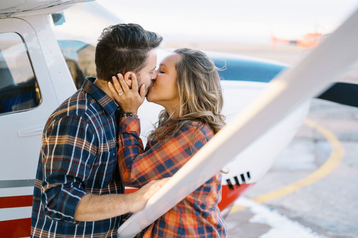Romantic moment shared between couple next to small aircraft.