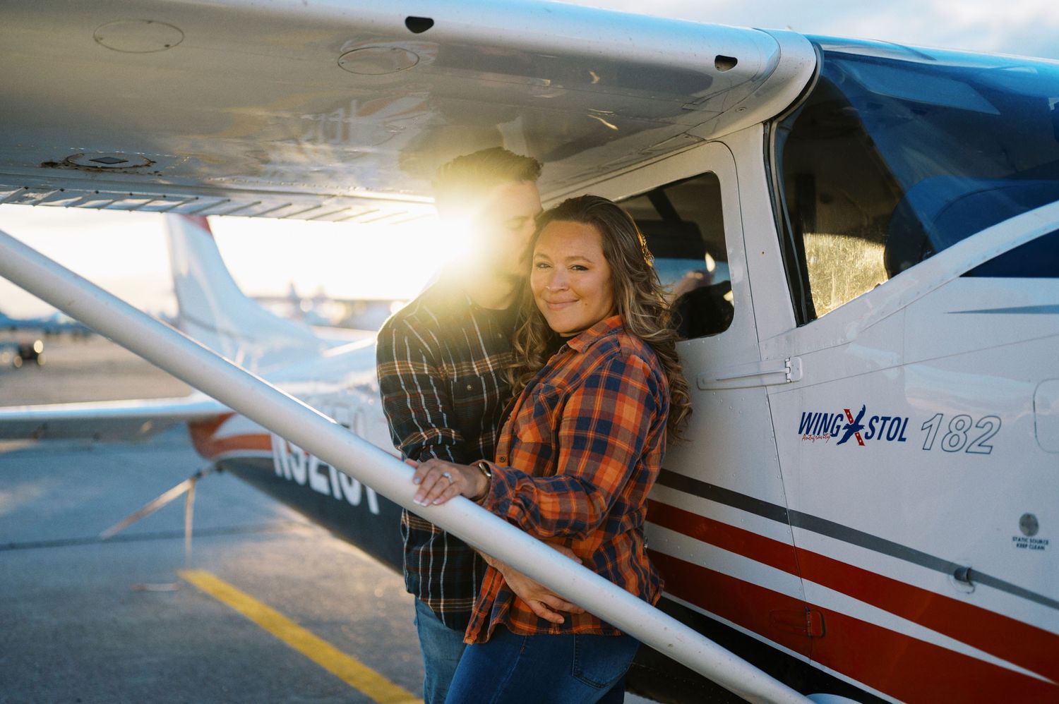 A person in a plaid shirt sits in the cockpit of a small private aircraft during golden hour.