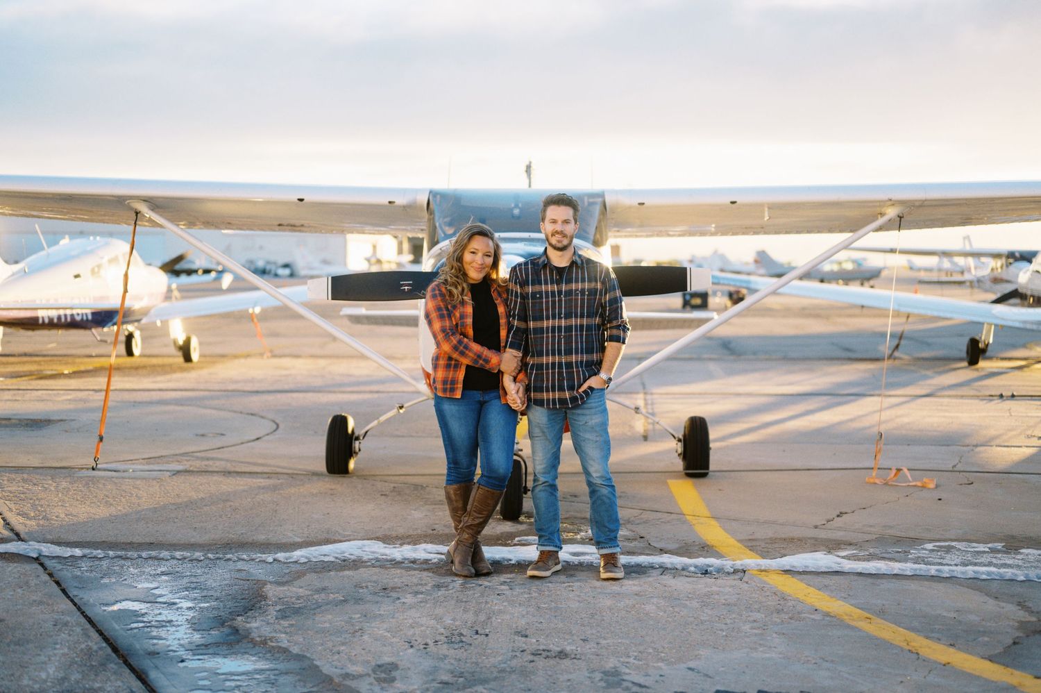 A couple stands together in front of a small private aircraft on an airport tarmac.
