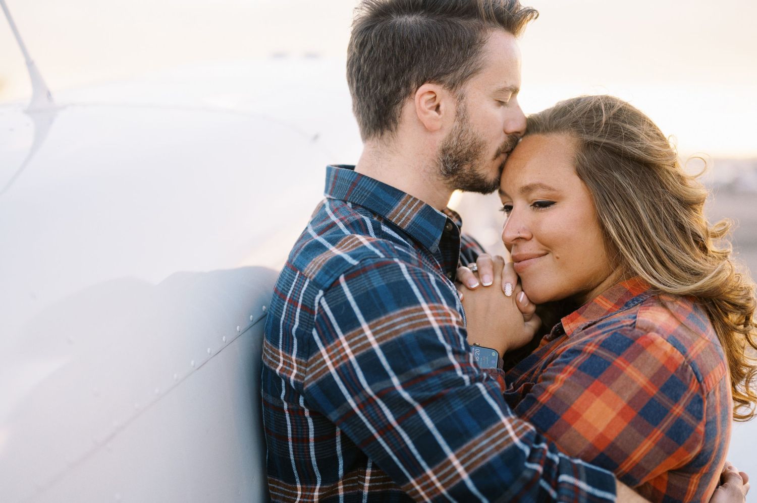 A romantic moment shared between a couple next to a small aircraft.