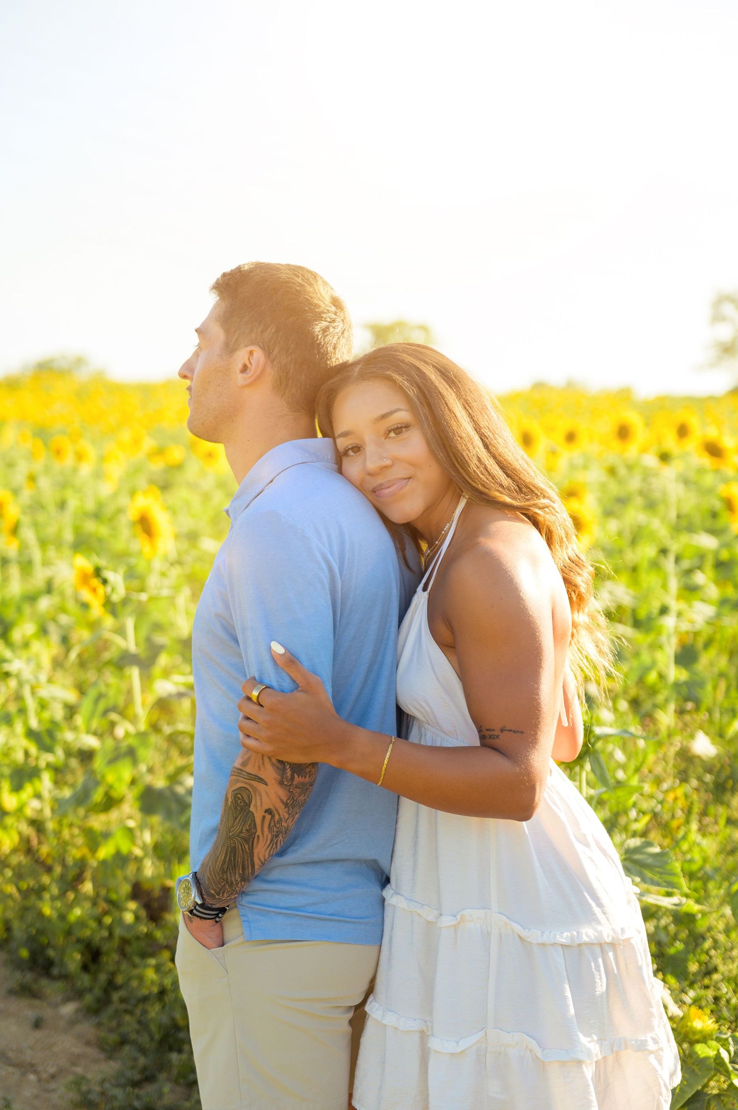 A couple embraces tenderly in a sunlit field of yellow flowers during golden hour.
