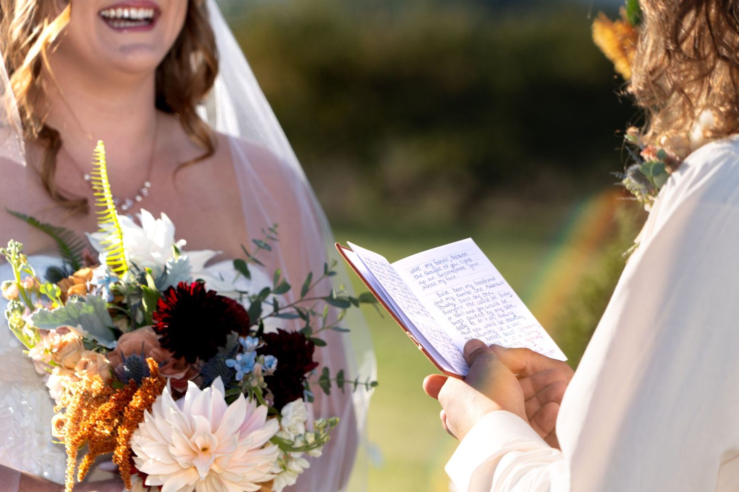 Close-up view of wedding ceremony with bouquet of blush dahlias and autumn wildflowers while vows are being read.