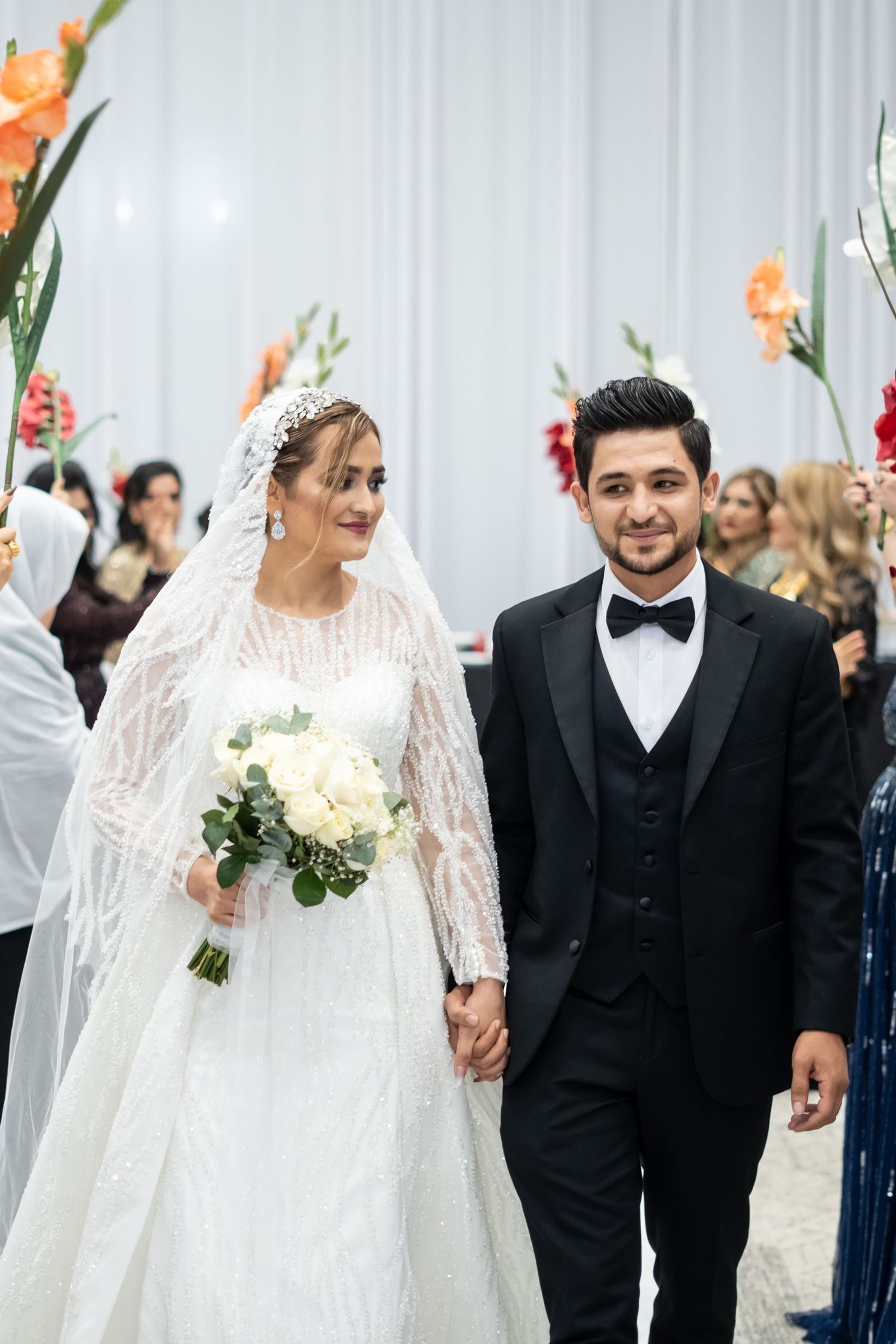 A happy wedding couple holds hands and walks together while wearing elegant white gown and classic black tuxedo.