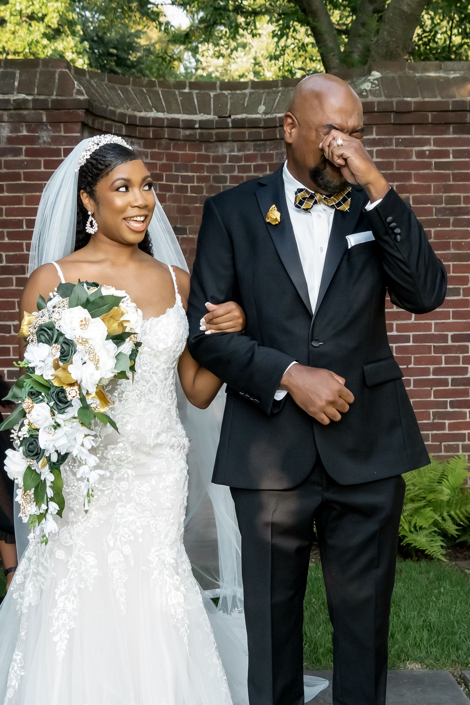 A joyful wedding couple shares a candid moment together in front of a brick wall during their outdoor photo session.