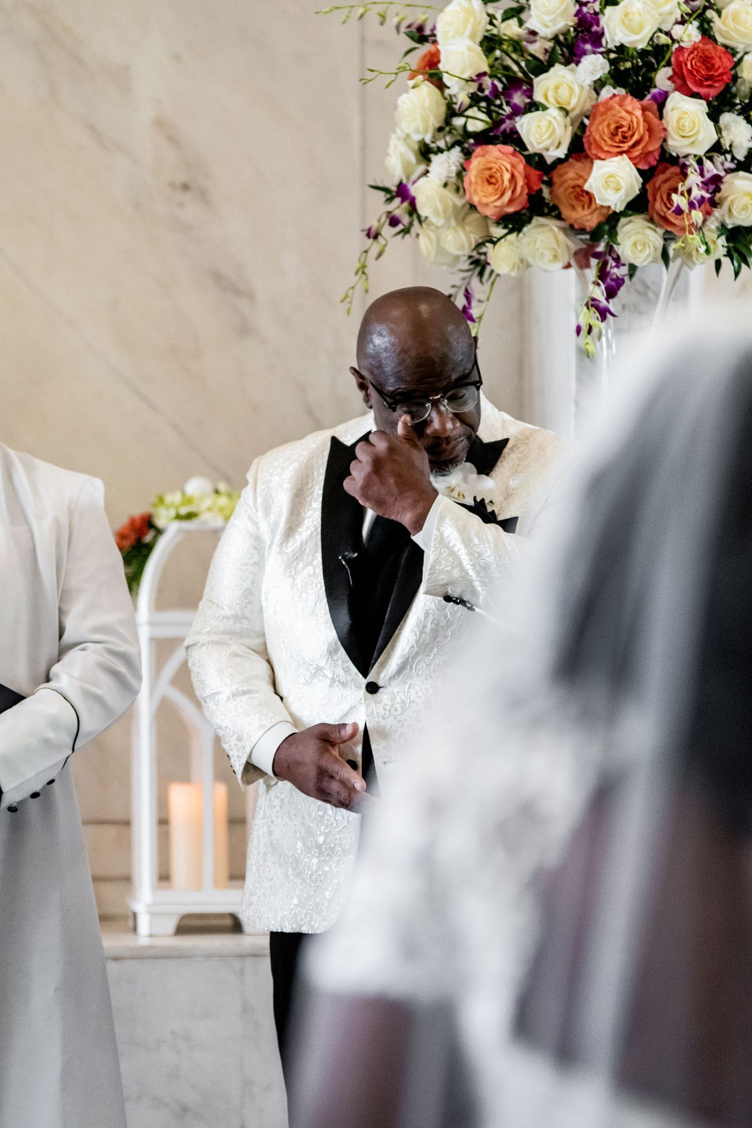 Beautiful wedding ceremony with white and coral floral arrangements as someone dabs tears during an emotional moment.