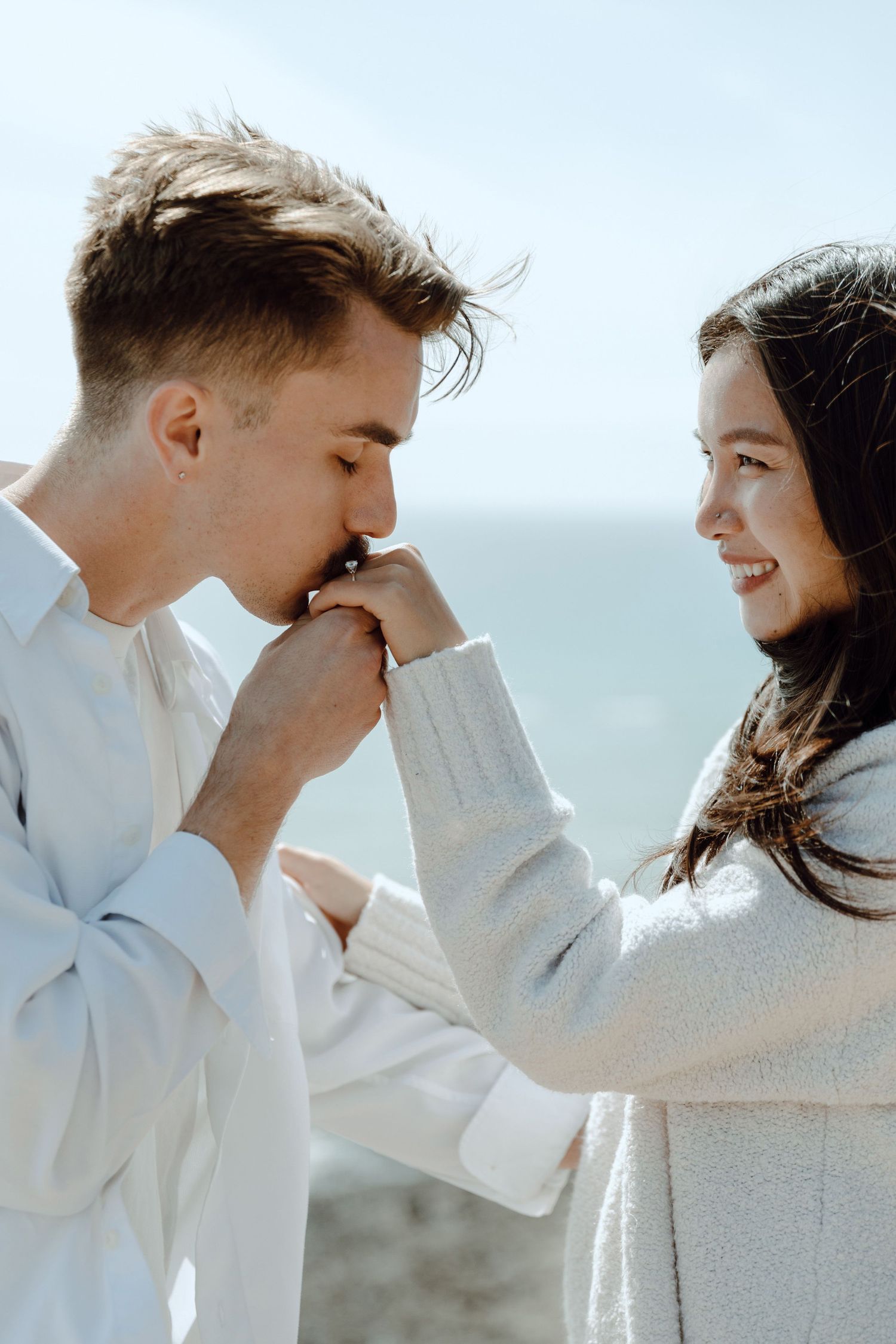 A couple shares a romantic moment on a cliff overlooking a beautiful coastal landscape at sunset.