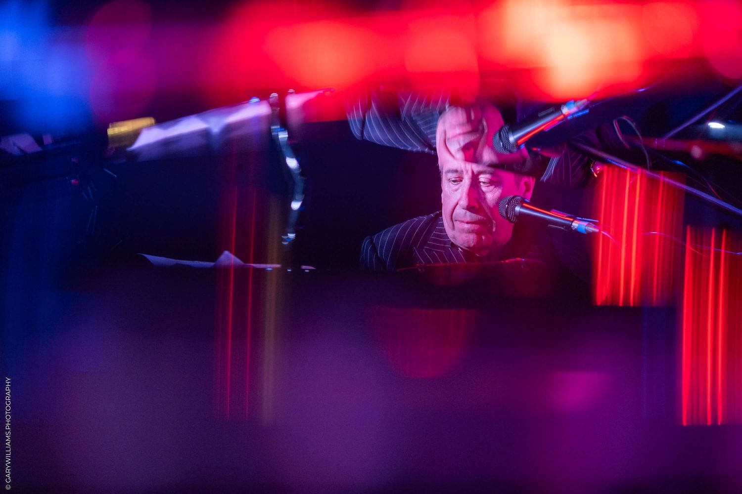 Stage performer seen through atmospheric lighting with blue and red hues during a live music show.