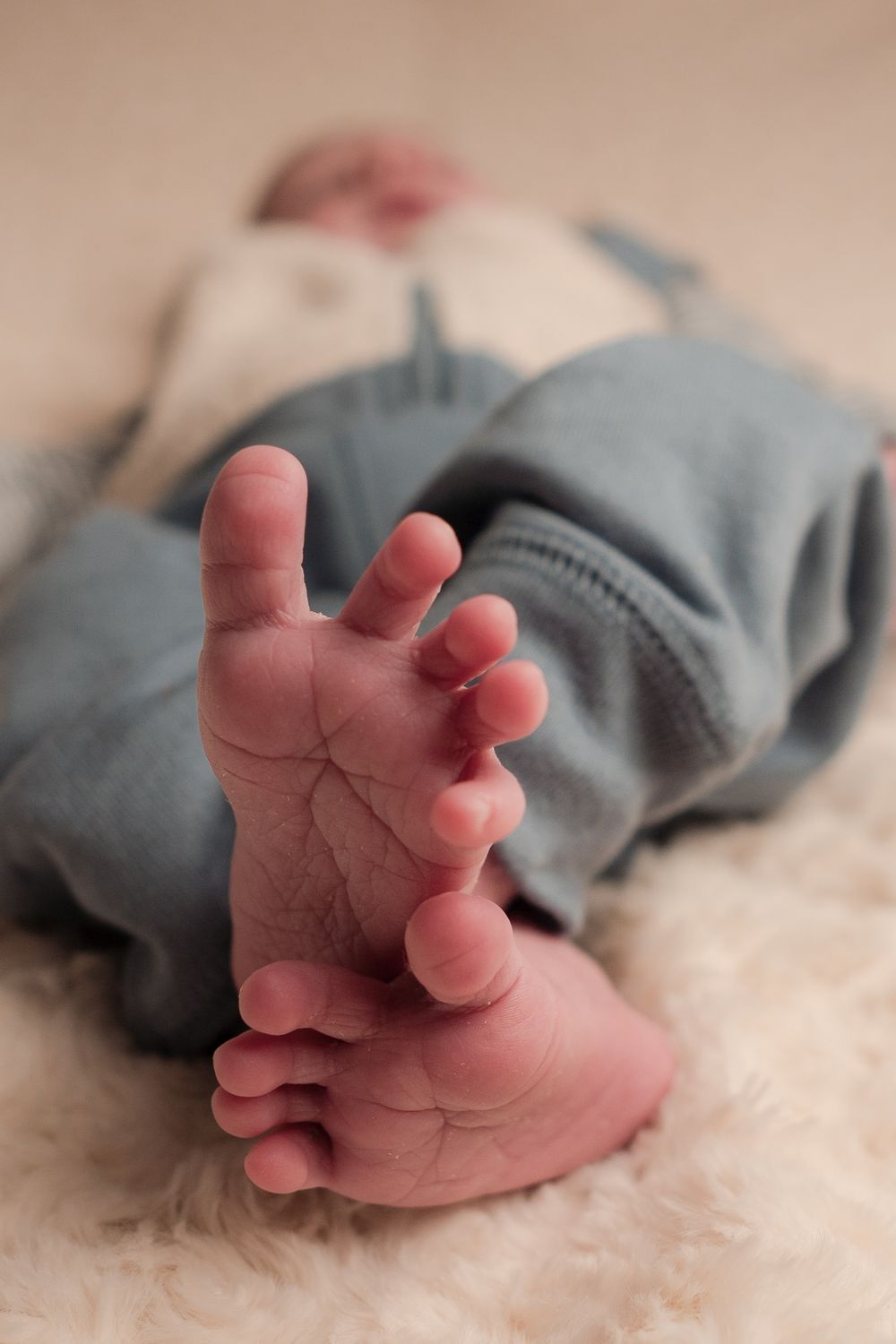 Close-up of tiny baby feet and toes against a soft white blanket, wearing grey clothing.