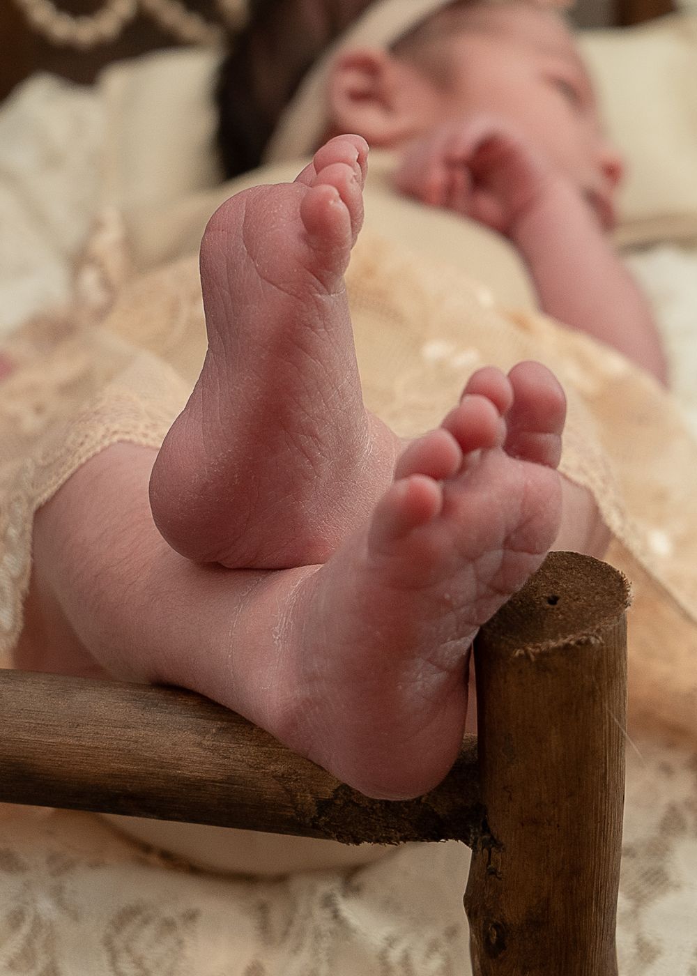 Close-up of tiny baby feet resting on a wooden armrest with delicate cream-colored lace fabric.