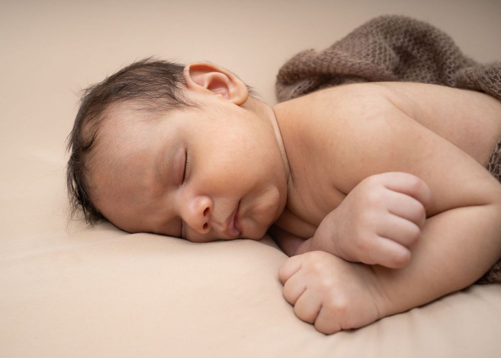 Peaceful sleeping newborn wrapped in a soft brown blanket on beige background.