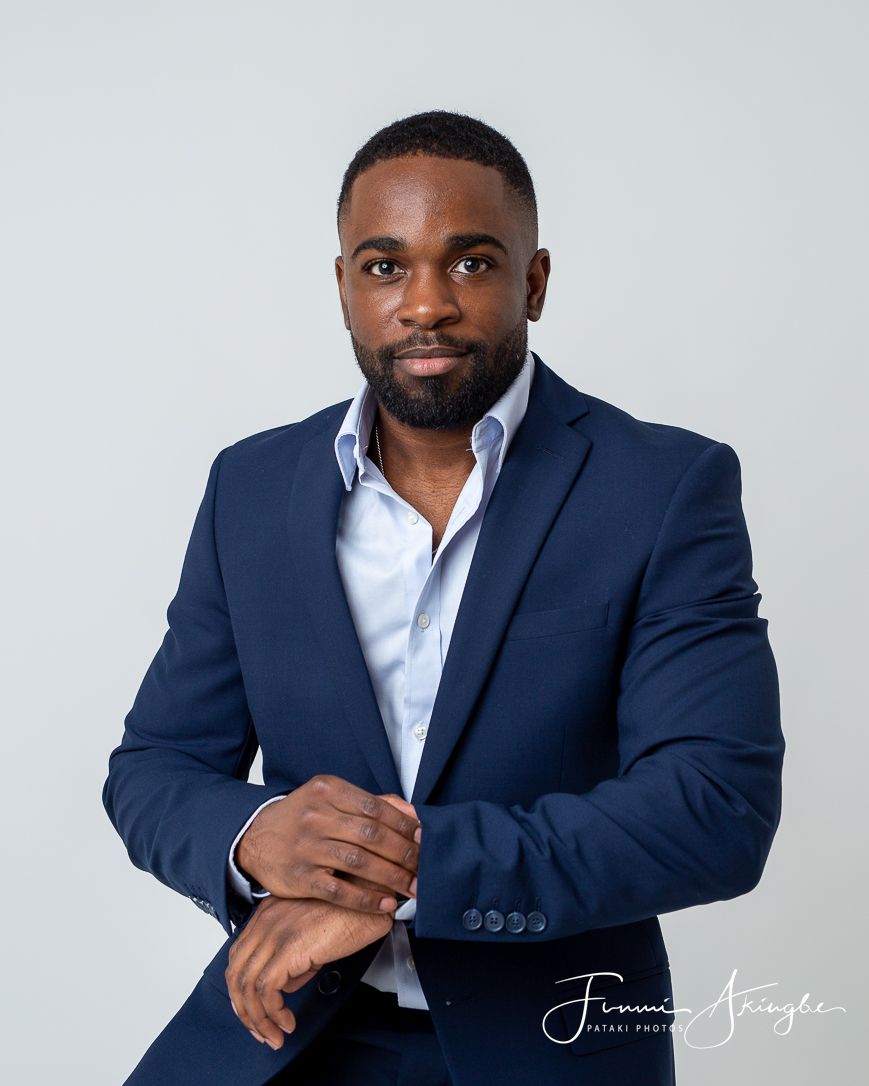 Professional business portrait of a young man in a navy suit and white dress shirt against a light grey background.