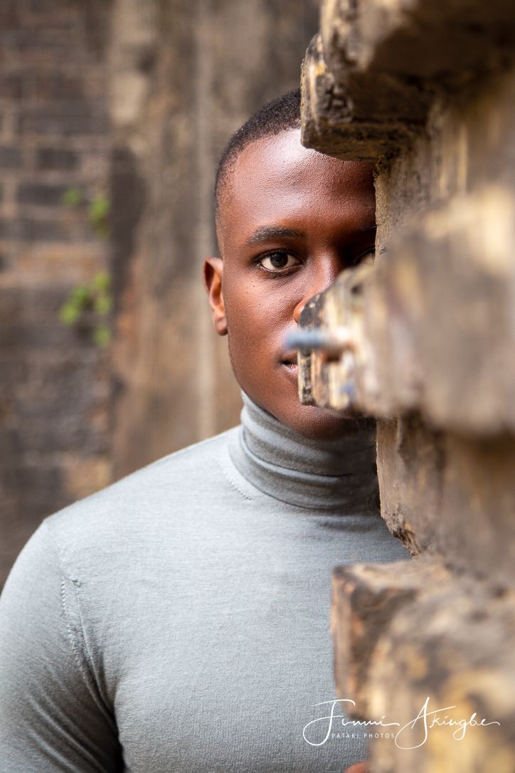 Creative portrait of a young man against a stone wall background with soft natural lighting and grey turtleneck sweater.