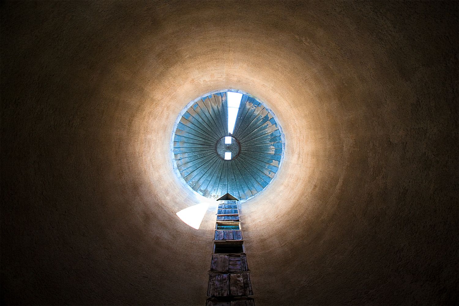 Looking up through a circular tunnel at a blue sky with industrial equipment visible.