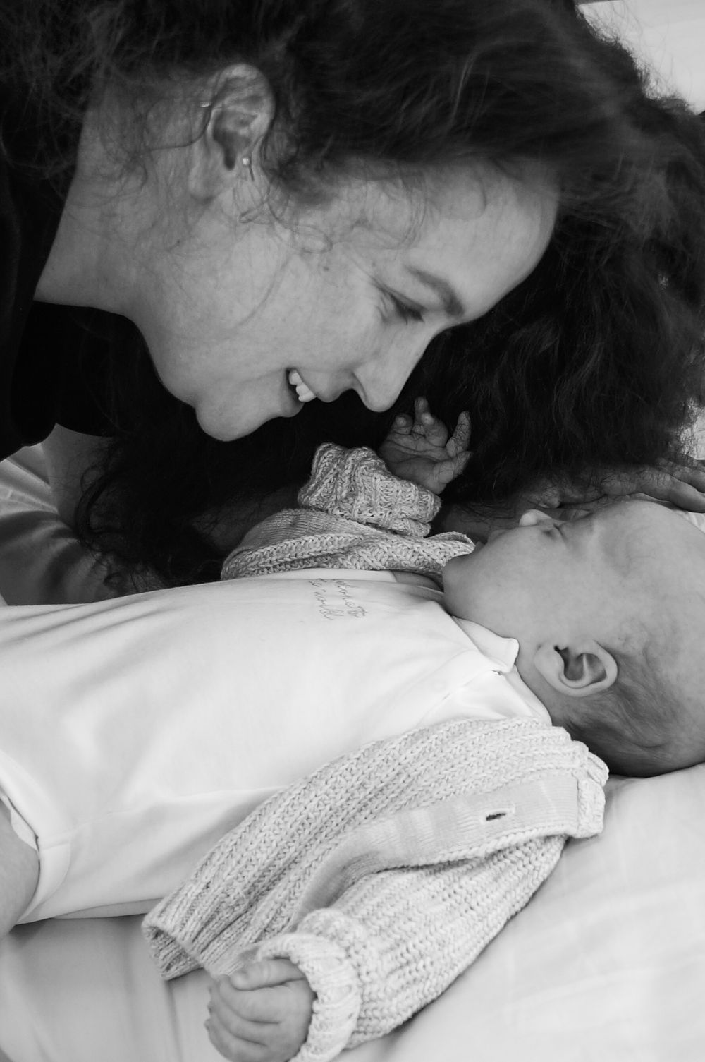 A tender black and white photograph showing a mother gazing lovingly at her infant wearing a knit sweater.