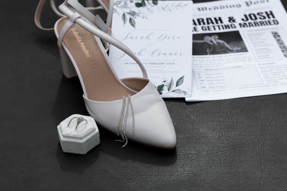White bridal shoe and hexagonal ring box displayed with wedding stationery.