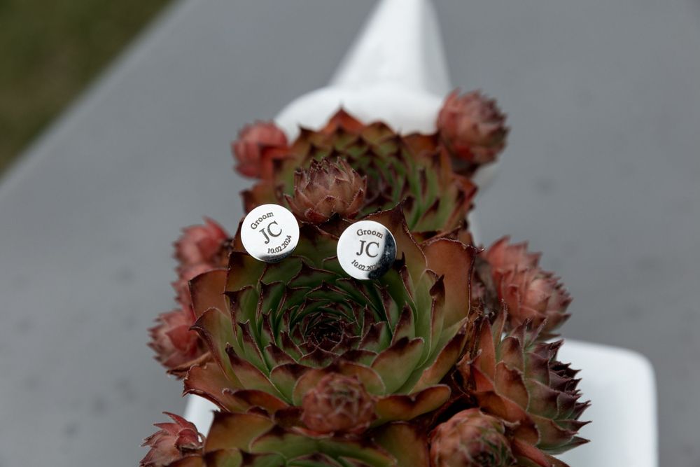Close-up of cufflinks sitting atop a burgundy succulent flower arrangement.