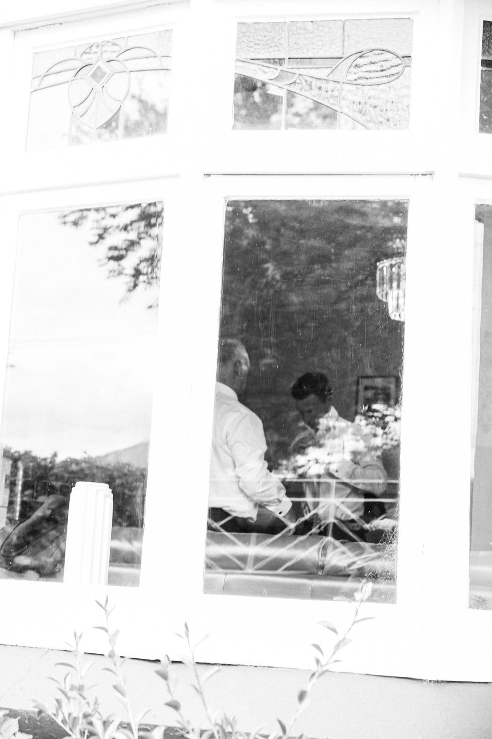 Black and white artistic window reflection showing landscape sketches and dining scene.