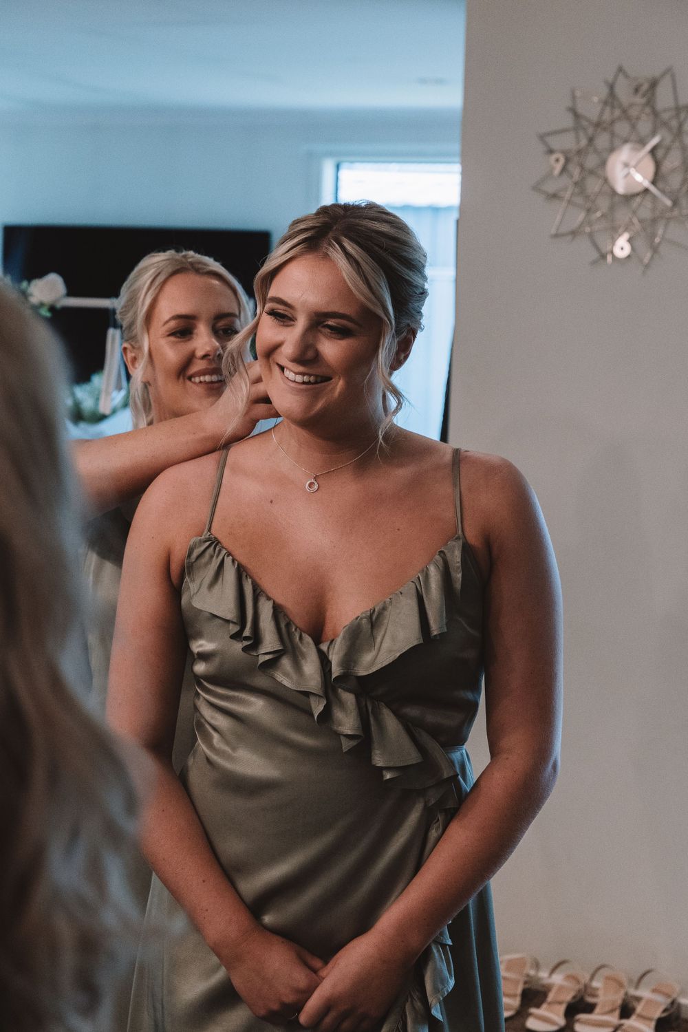 Bridesmaids in silk olive green dresses sharing a joyful moment during wedding preparations.