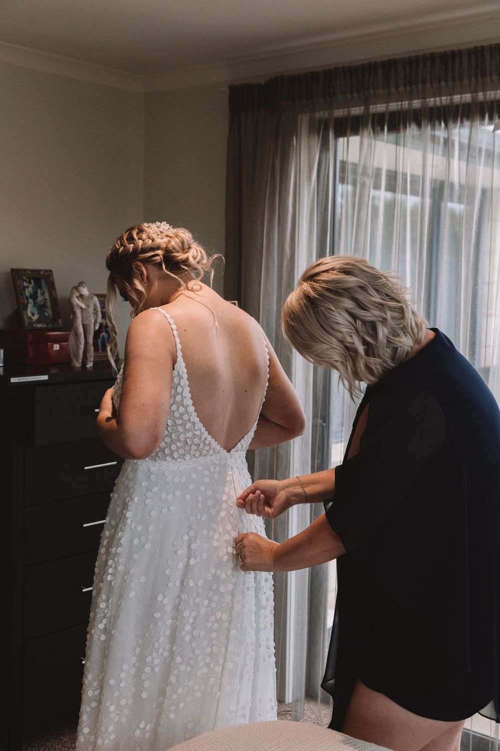 Final adjustments being made to a sparkly white wedding dress before the ceremony.