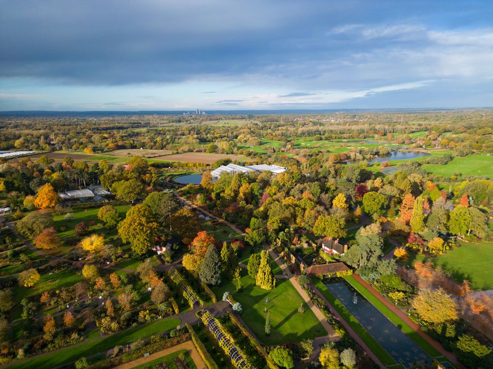 Aerial autumn view of green countryside with winding river, colorful fall trees, and scattered homes under cloudy skies.