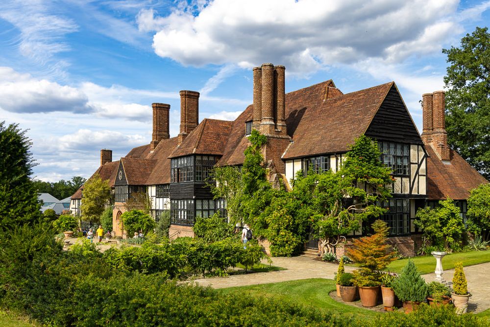 A panoramic view of traditional English Tudor-style homes with timbered walls and rustic gardens under cloudy skies.