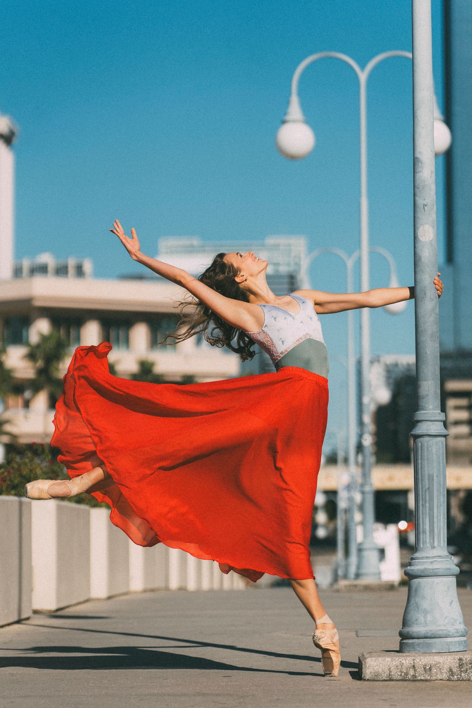 tampa bay dance photoshoot of a ballerina on a bridge holding onto a lamp post in vibrant red skirt and pointe shoes