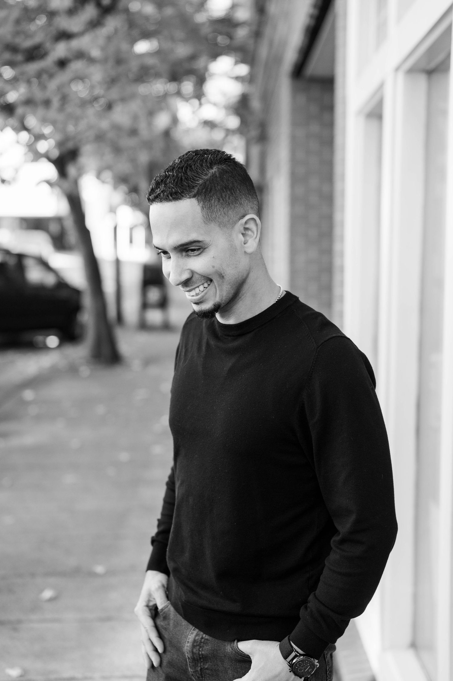 Black and white portrait of someone in a casual black sweater smiling while looking down outdoors.
