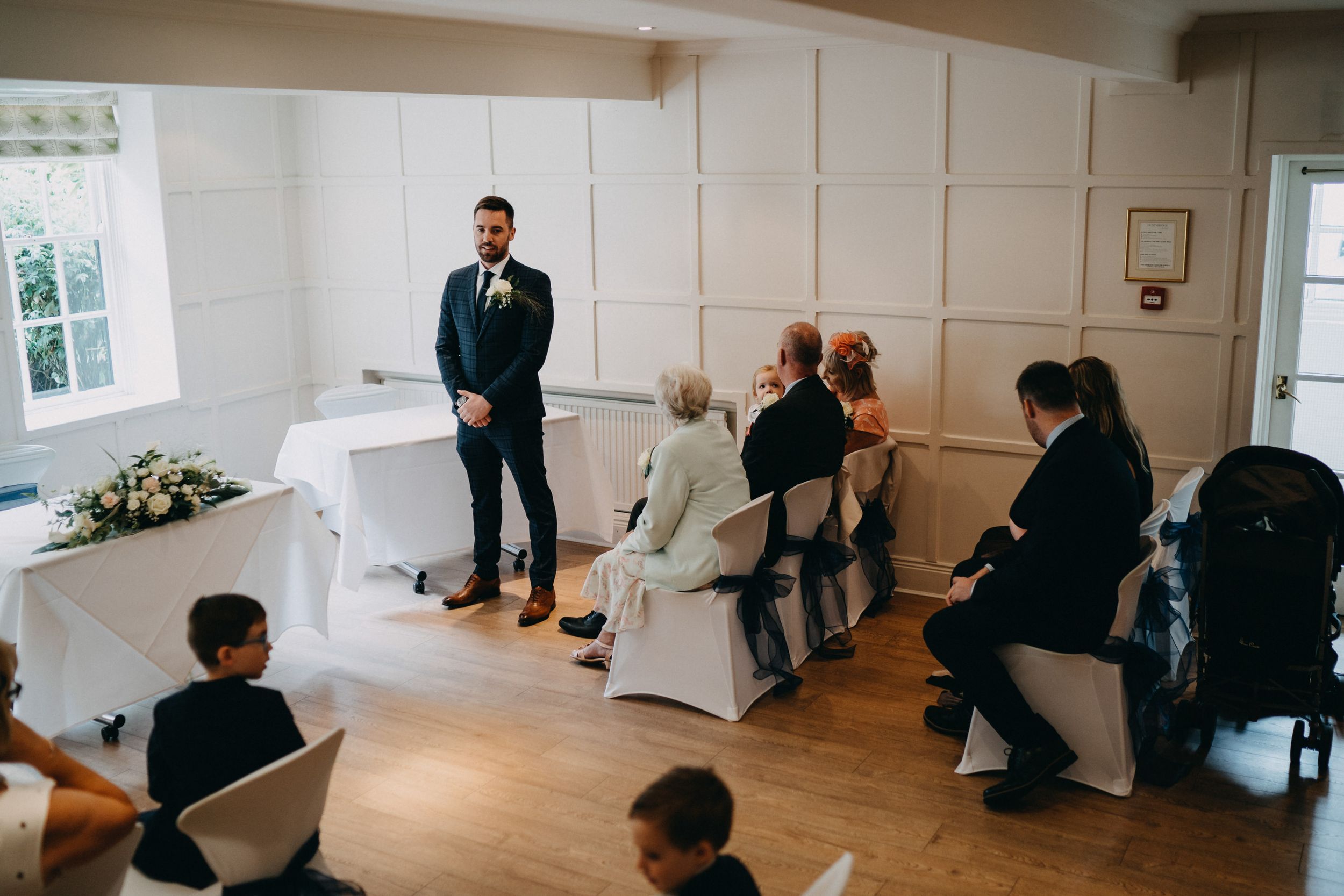 An intimate indoor wedding ceremony at The Old Bridge in a bright room with wooden floors and white chairs.