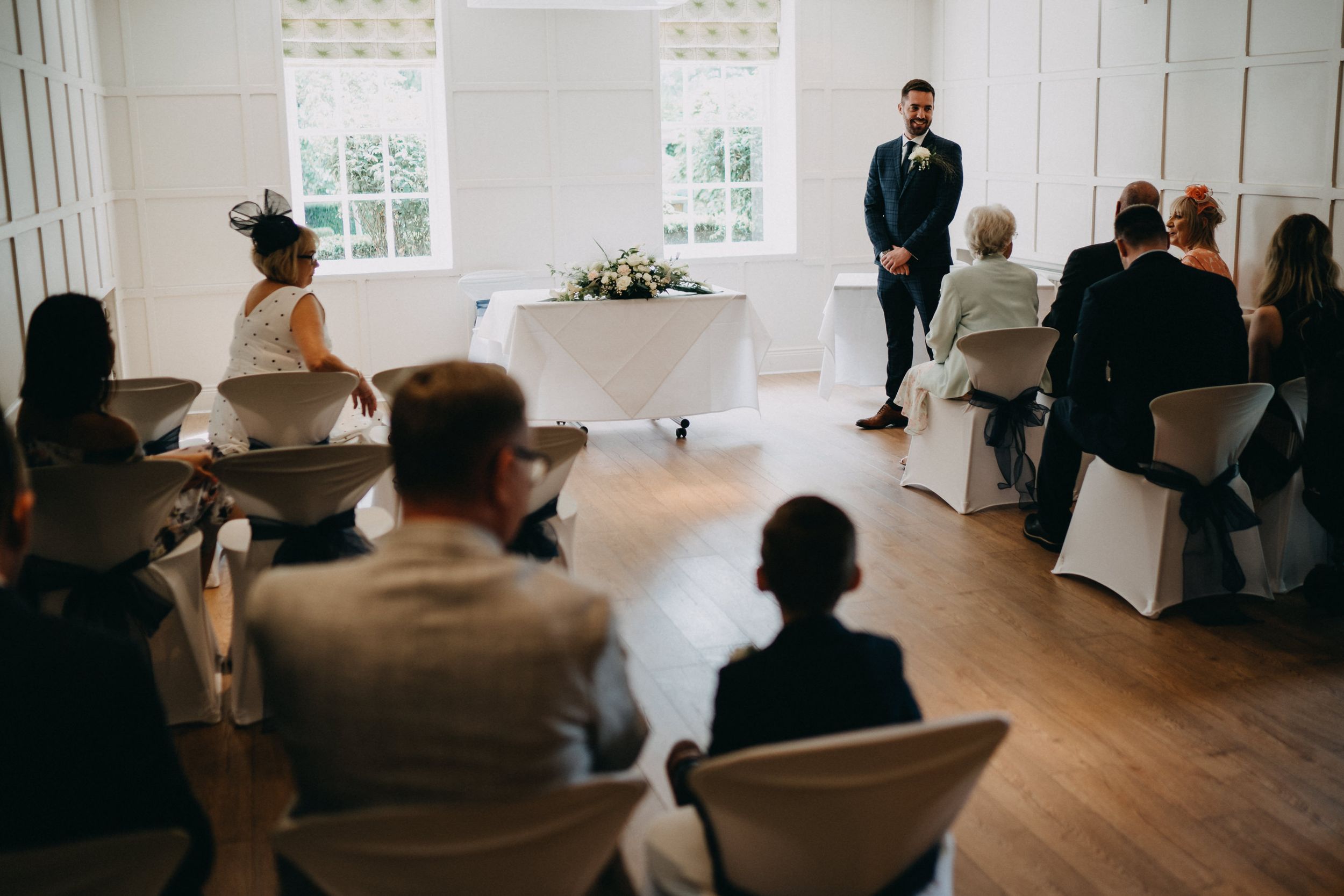 Small intimate wedding ceremony taking place in a bright white room with hardwood floors and windows.