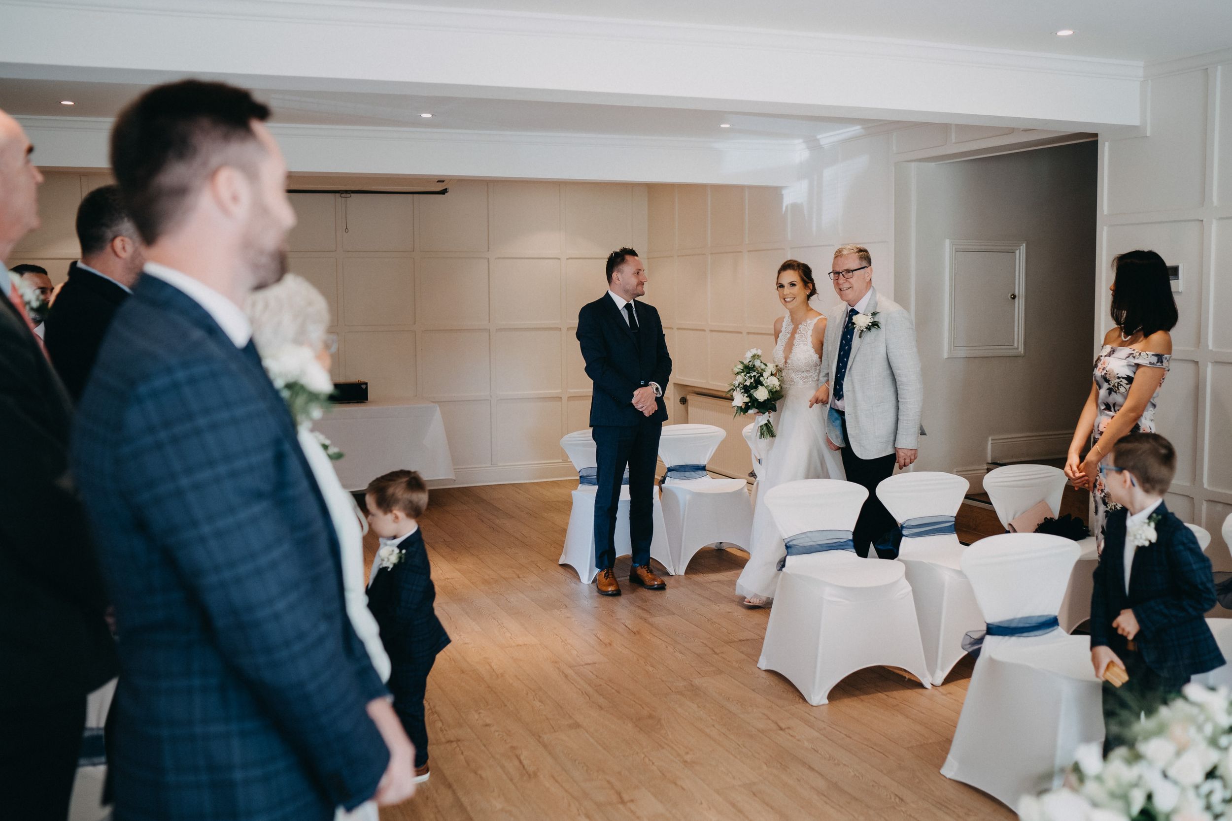 A small wedding gathering in a modern room of The Old Bridge, Huntingdon with hardwood floors and white chairs arranged for the ceremony.