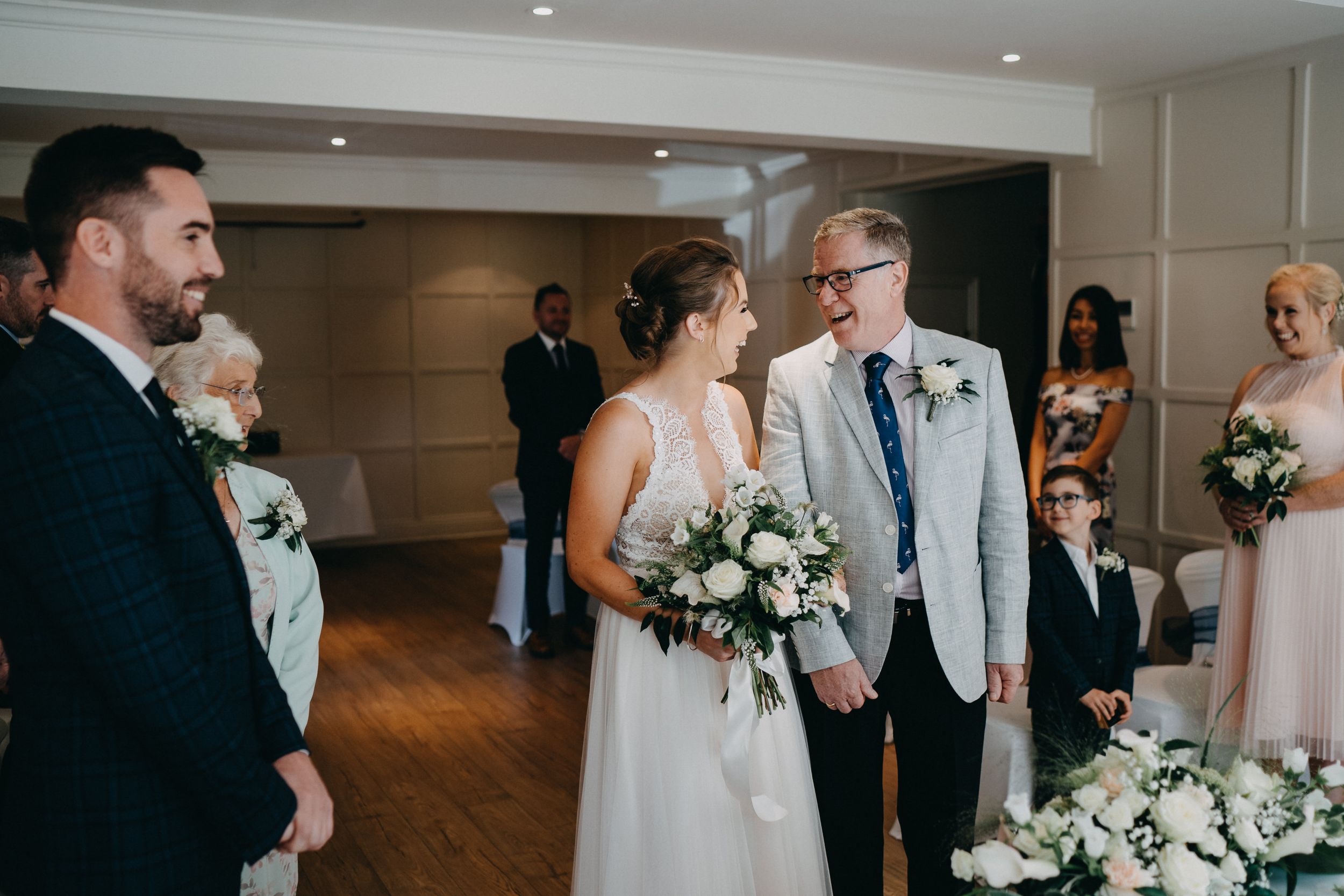 A joyful wedding ceremony moment in an elegant indoor venue with white floral arrangements and soft lighting.