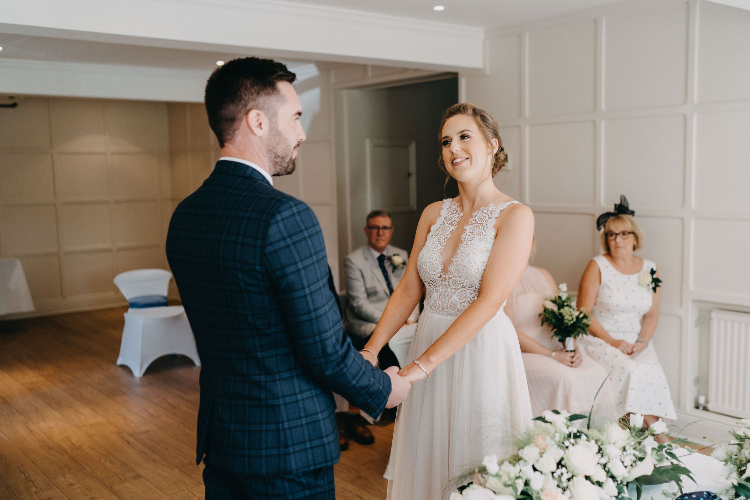 A couple shares a joyful moment during their wedding ceremony in an elegant room with white decor and wooden floors.