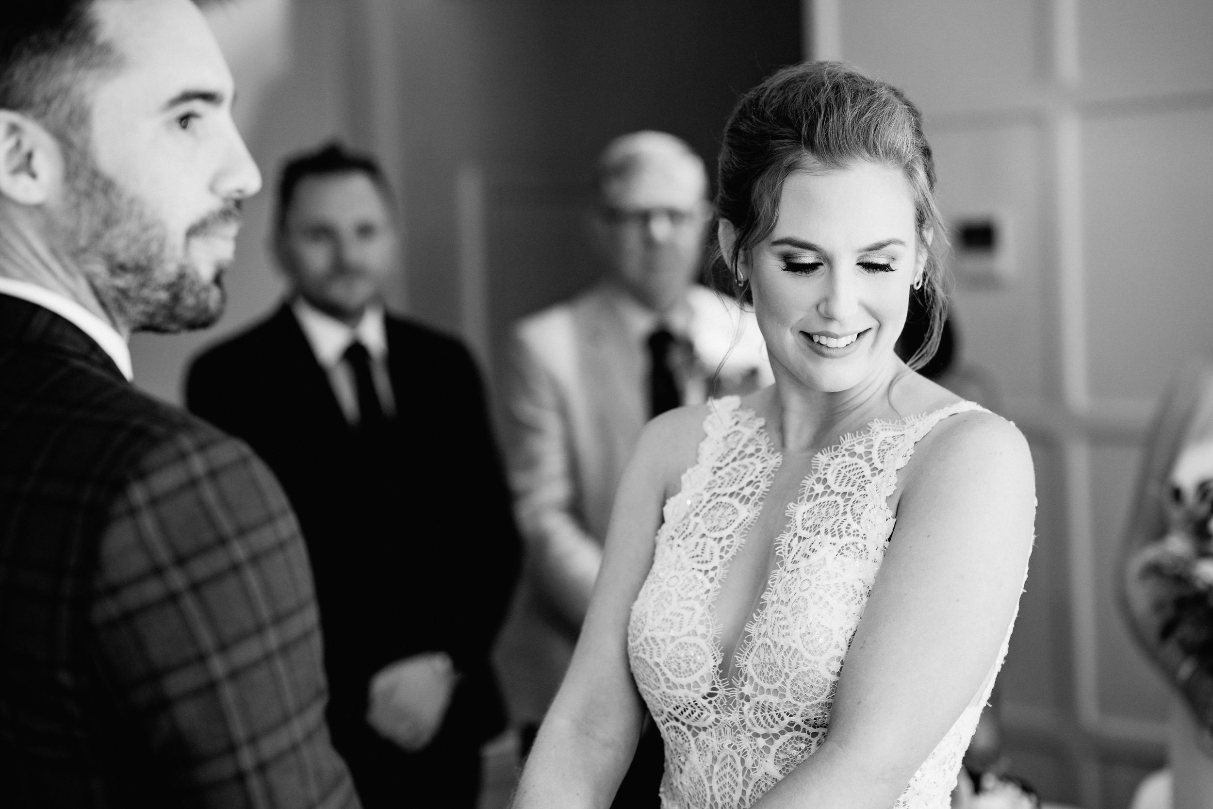 Black and white photo of a couple at a wedding ceremony, with the bride wearing an elegant lace gown.